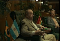two men sitting in chairs with flags in front of them
