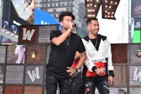 two men are singing into a microphone in front of a building
