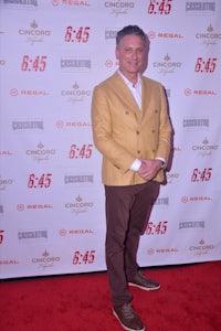 a man in a tan jacket standing on a red carpet