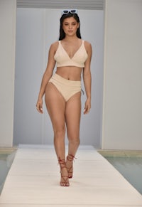a model walks the runway in a beige bikini and sandals